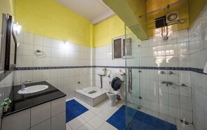 A bathroom with a sink, toilet, and shower area, featuring white and blue tiles and a yellow wall. - India Hotel (Nainital)