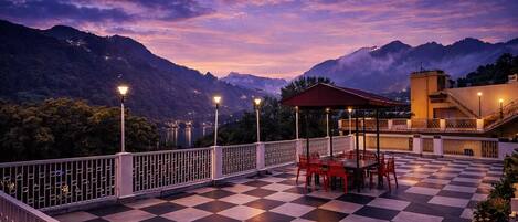 A terrace with a checkered floor, outdoor seating, and a view of mountains.
