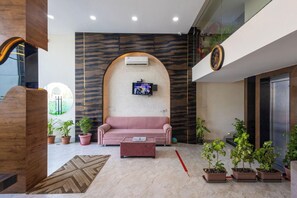 A modern lobby with a sofa, coffee table, potted plants, and a mounted TV. - Hotel Aranyasutra Inaya Indore (Indore)