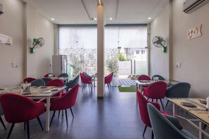 A modern dining area with tables and chairs, a visible outdoor view, and ceiling fans. - Hotel Aranyasutra Inaya Indore (Indore)