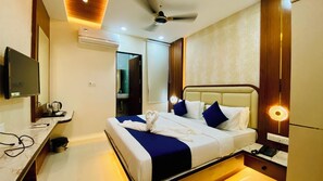 A hotel room with a bed, bedside table, TV, and a ceiling fan. - Hotel Aranyasutra Inaya Indore (Indore)