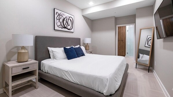 A modern bedroom with a large bed, bedside tables, a mirror, and a wall art piece.