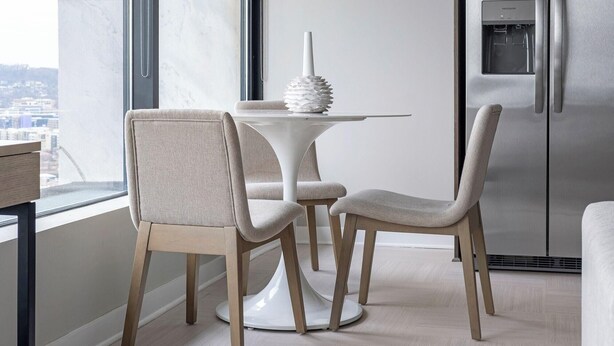 Eine moderne Küche mit einem weißen Tisch und Stühlen, einer dekorativen Vase und einem Edelstahl-Kühlschrank.