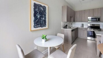 A modern kitchen with a dining area, featuring a white table, grey chairs, and a potted plant.