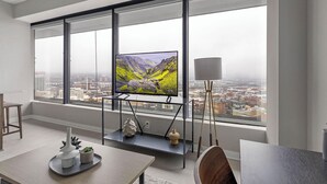 Ein modernes Zimmer mit großem Fenster, Flachbildfernseher, Esstisch und Lampe.