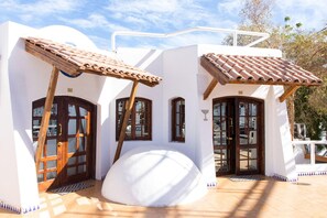 Un edificio blanco con dos puertas y ventanas de madera, un tejado de tejas, y una estructura esférica blanca en el centro.