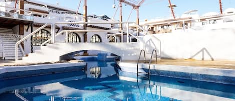 A swimming pool with a diving board, a staircase, and a white building with arches.