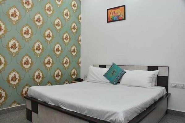 A bed with white bedding, a single pillow, and a decorative pillow on a wall with a patterned wallpaper. - Ramas Resort (Jaipur)