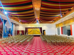 A large hall with rows of chairs, a stage with a golden backdrop, and a red carpet. - Ramas Resort (Jaipur)