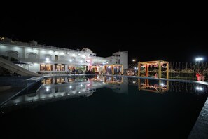 Un hôtel doté d’une piscine qui reflète le bâtiment et d’un espace couvert illuminé.