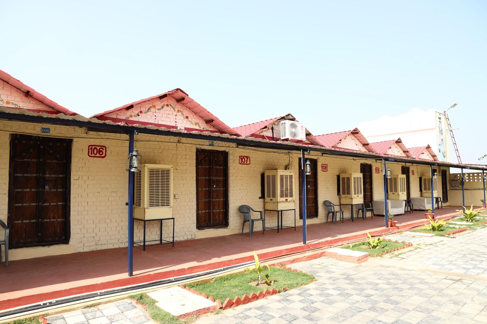 A row of numbered rooms with air conditioning units, a small garden area, and a clear sky.