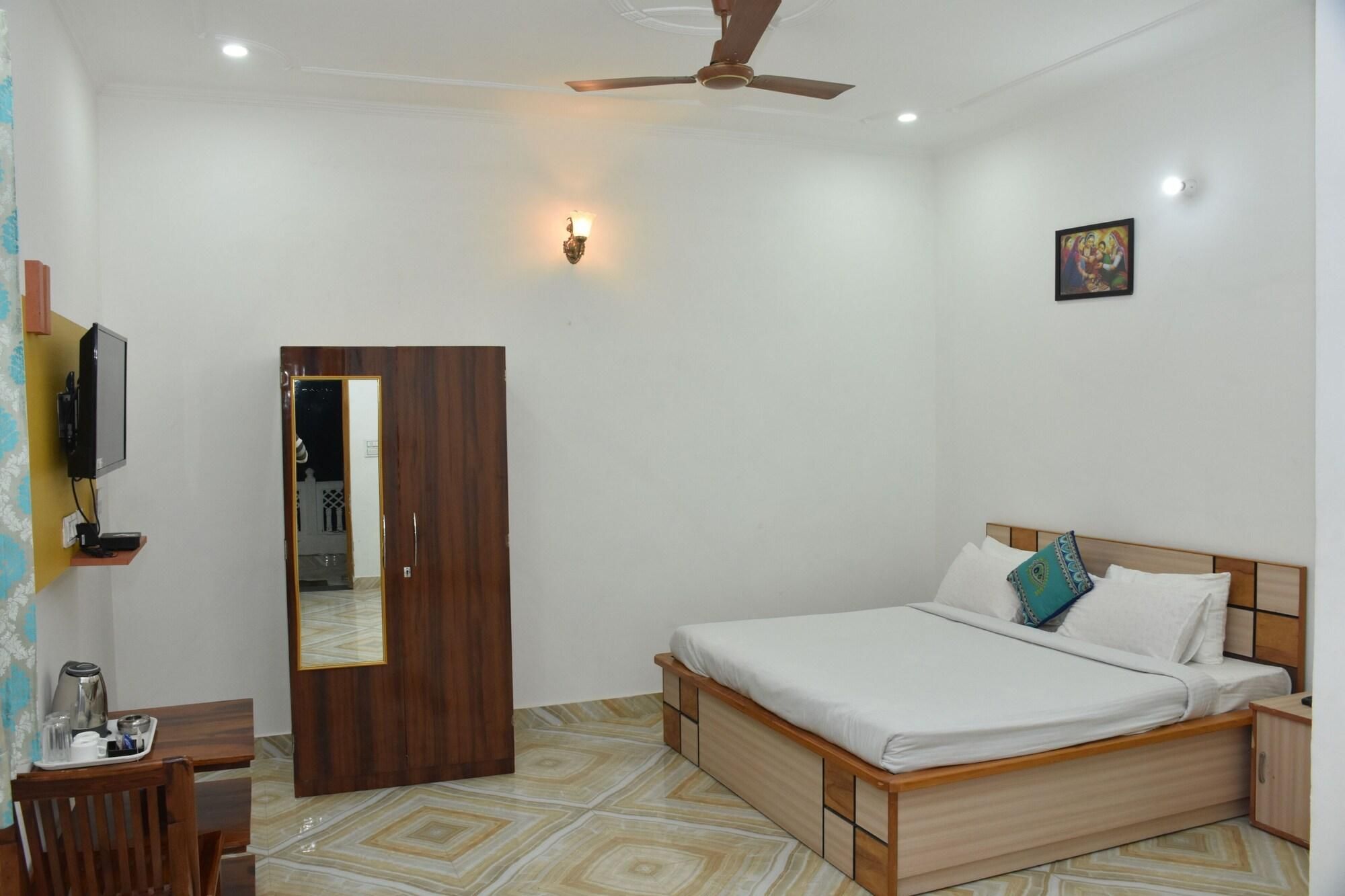 A bedroom with a bed, a wooden wardrobe, a desk with a chair, a television, and a ceiling fan.