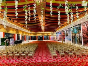 A large hall with rows of chairs, a red carpet, and hanging white flowers. - Ramas Resort (Jaipur)