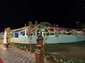 A well-lit outdoor area with a covered seating area, decorative plants, and a pathway leading to the entrance. - Ramas Resort (Jaipur)