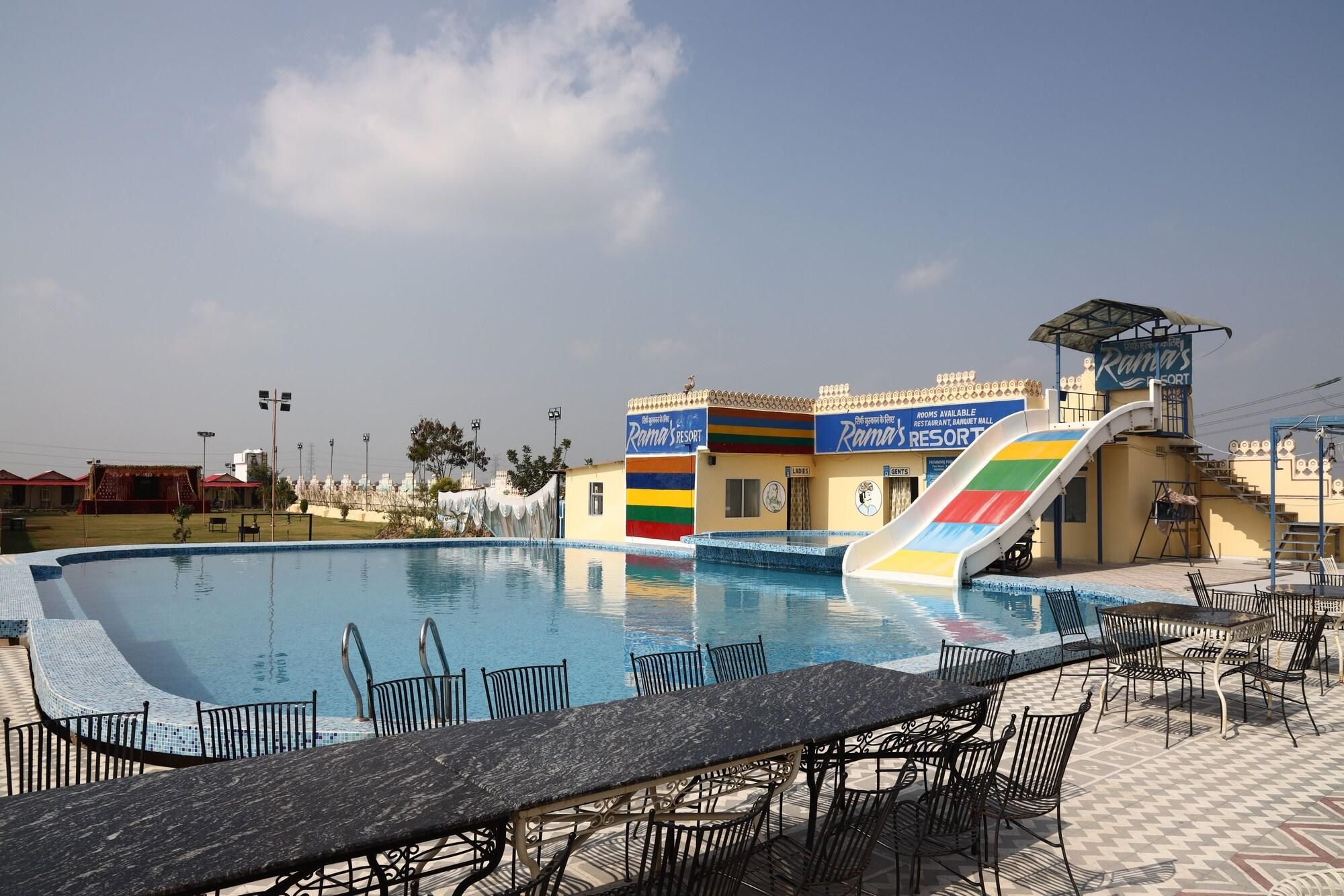 A pool area with lounge chairs and tables, a slide, and a building with a colorful facade.