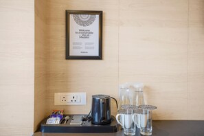 Un cartel de bienvenida enmarco, una tetera, una cafetera, un sobre de azúcar y dos vasos sobre una mesa.