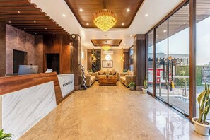 Vestíbulo de hotel con mostrador de recepción, candelabro, conjunto de sofás y un amplio ventanal con vistas.