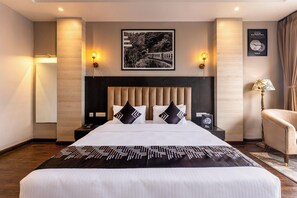 A hotel room with a large bed, a headboard, two bedside lamps, a nightstand, a chair, and a framed picture on the wall. - Medalio Boutique Orbit International (Gangtok)