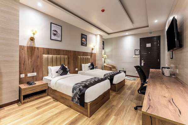 Hotellihuone, jossa on kaksi sänkyä, työpöytä, tuoli, televisio ja ovi.