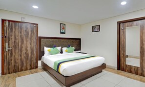 A hotel room with a wooden headboard, a bed with white bedding and colorful pillows, a nightstand, and a wooden wardrobe. - Treebo Vetri Supreme Residency (Chennai)