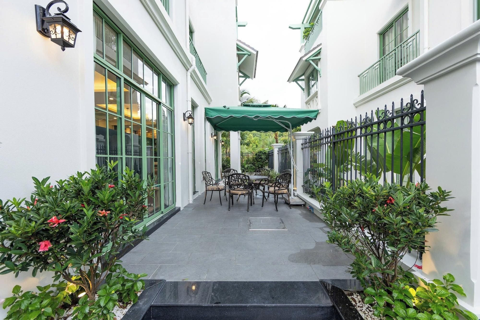 A narrow outdoor corridor with a green canopy, outdoor seating, and a gated entrance.