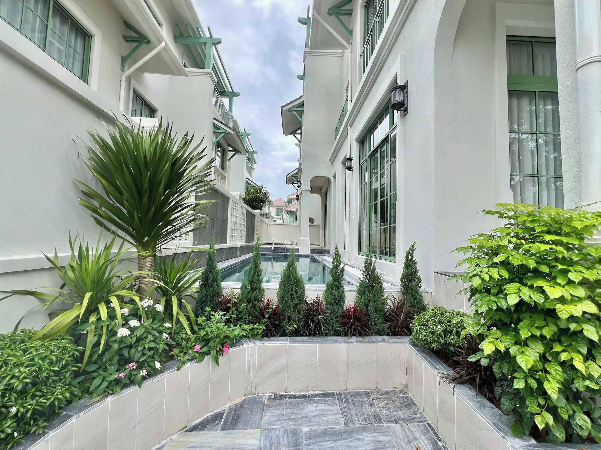 A hotel corridor with a pool, potted plants, and a tiled floor.