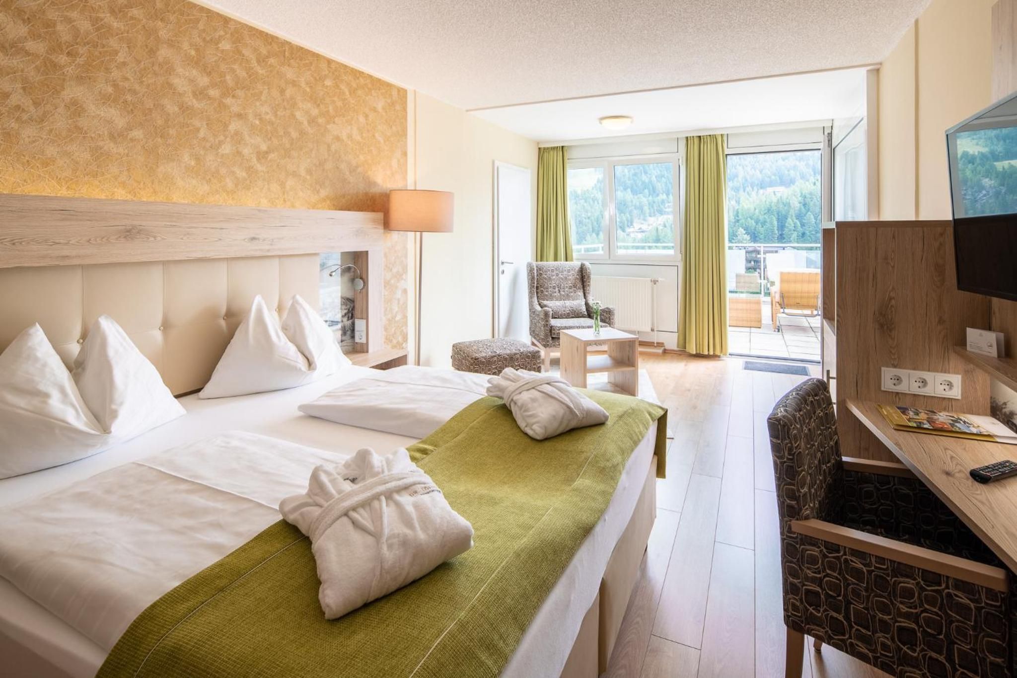 Een hotelkamer met twee bedden, een bureau met een computer, een stoel en uitzicht op groen.