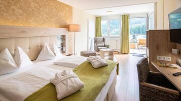 Een hotelkamer met twee bedden, een bureau met een computer, een stoel en uitzicht op groen.