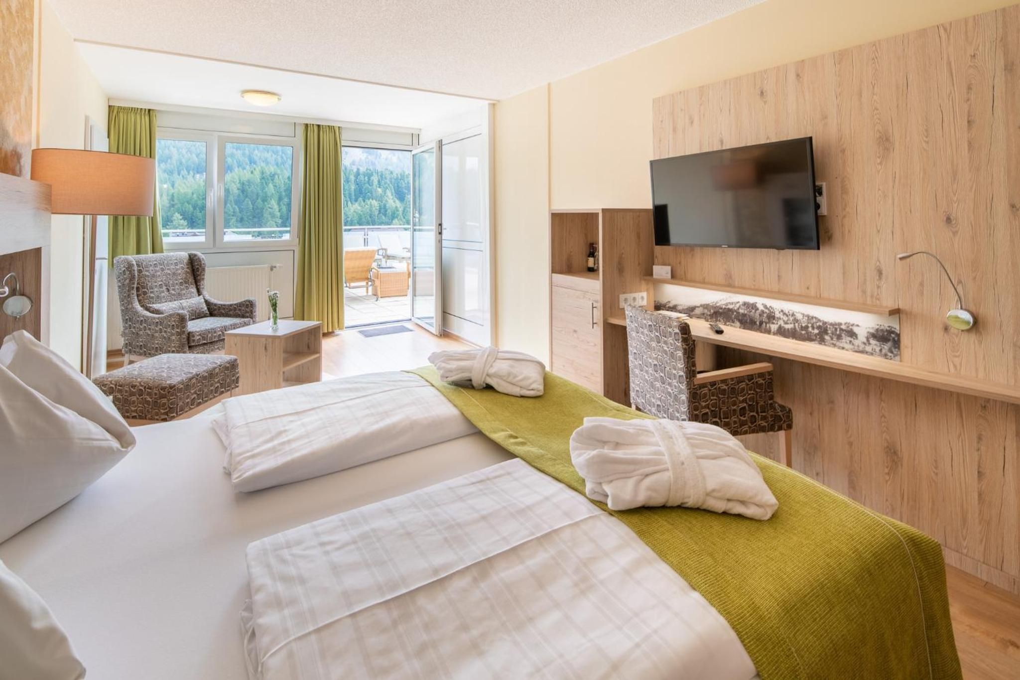 Een hotelkamer met een bed, bureau, stoel, televisie en uitzicht op de omgeving.