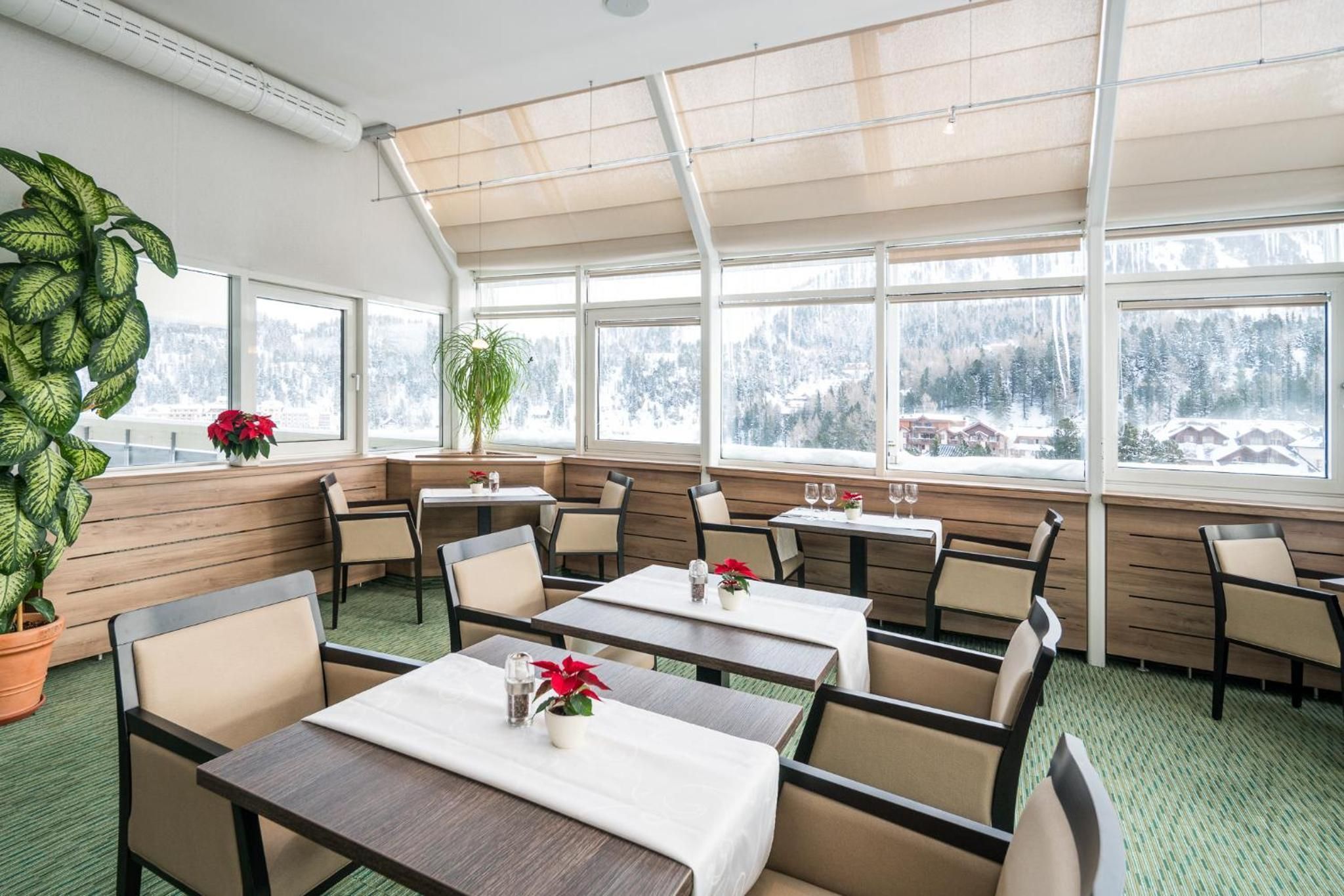 A restaurant with a high ceiling and large windows, offering views of a snowy landscape.