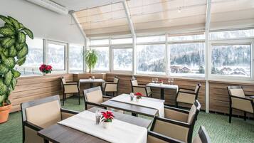 A restaurant with a high ceiling and large windows, offering views of a snowy landscape.