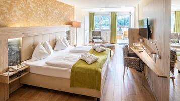 A hotel room with a bed, bedside tables, a desk, a chair, a TV, and a view of the outdoors.