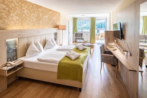 Habitación de hotel con cama, mesitas de noche, escritorio, silla, televisor y vistas al exterior.