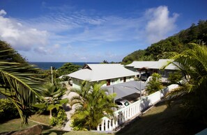 A coastal property with multiple buildings, a white fence, and lush greenery. - Surfers Self Catering Chalets (Mahé Island)
