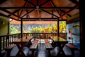A covered outdoor seating area with wooden benches and a view of a waterfall. - Surfers Self Catering Chalets (Mahé Island)