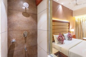 A hotel room with a shower, a bed with patterned pillows, and a nightstand with a lamp. - Hotel Supreme Comforts Mumbai Airport (Mumbai)