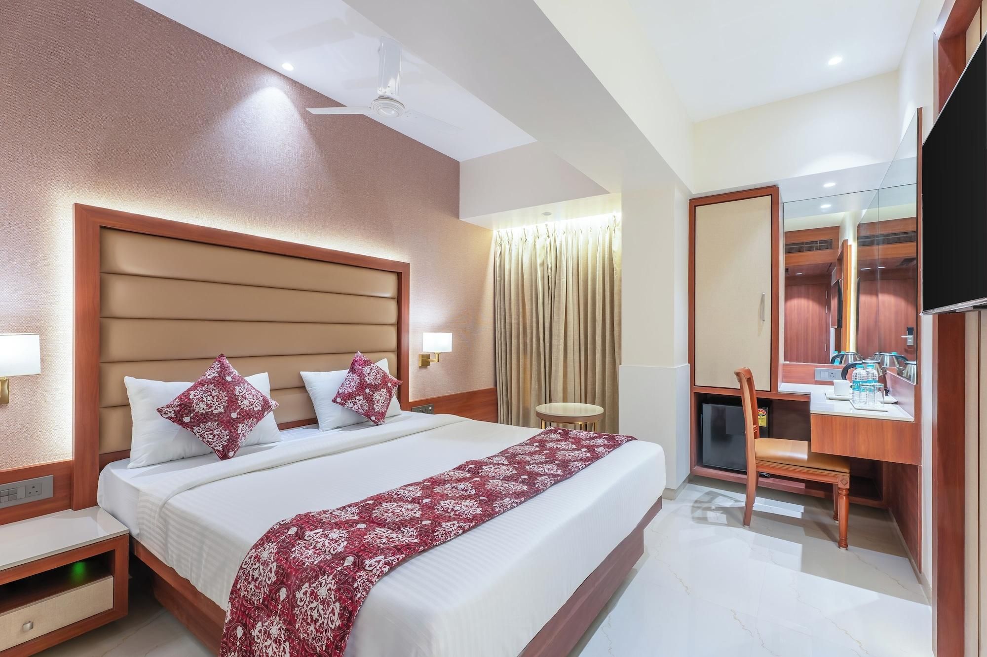 A hotel room with a large bed, a desk with a chair, a mirror, and a television.