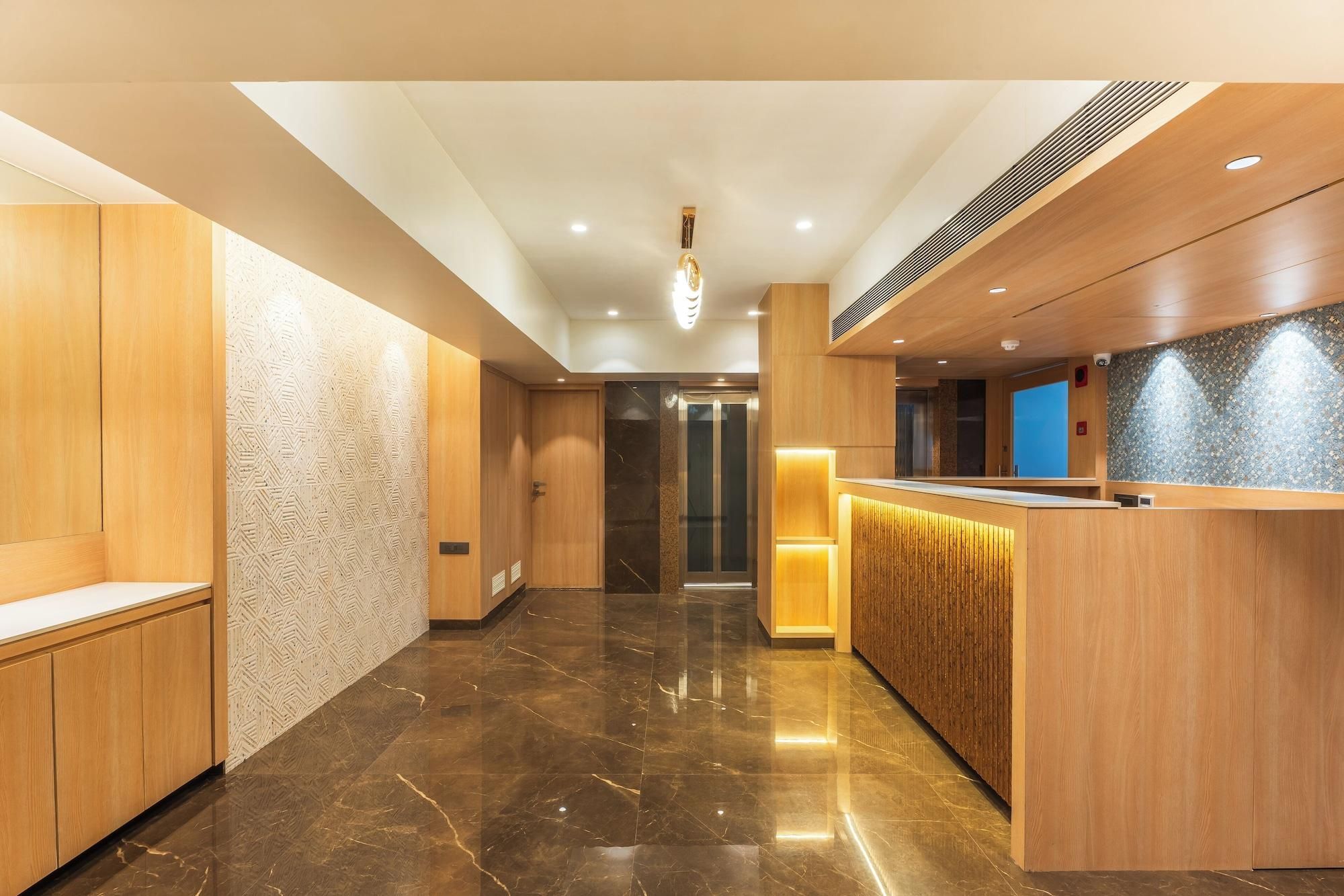 A hotel lobby with a reception desk, wooden paneling, a marble floor, and an elevator.