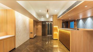 A hotel lobby with a reception desk, wooden paneling, a marble floor, and an elevator.