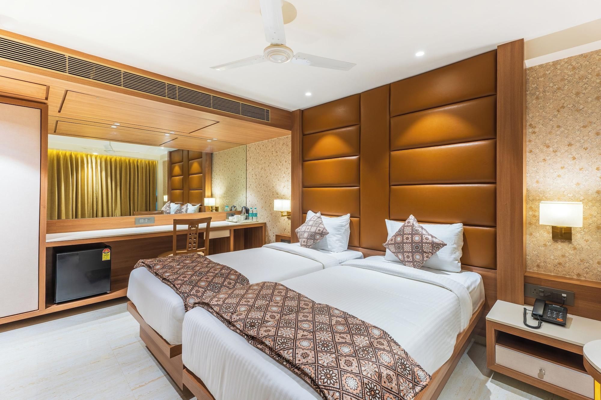 A hotel room with a large bed, a desk, a chair, a mirror, a ceiling fan, and a small refrigerator.