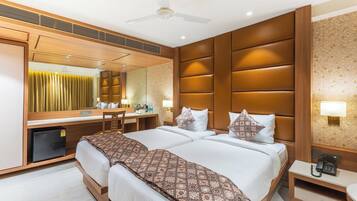 A hotel room with a large bed, a desk, a chair, a mirror, a ceiling fan, and a small refrigerator.