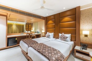 A hotel room with a large bed, a desk, a chair, a mirror, a ceiling fan, and a small refrigerator. - Hotel Supreme Comforts Mumbai Airport (Mumbai)