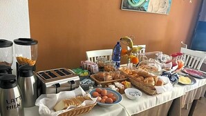 En morgenmadsbuffet med forskellige spiser, en brødrister og termokander mærket 'LATTE MILK'.