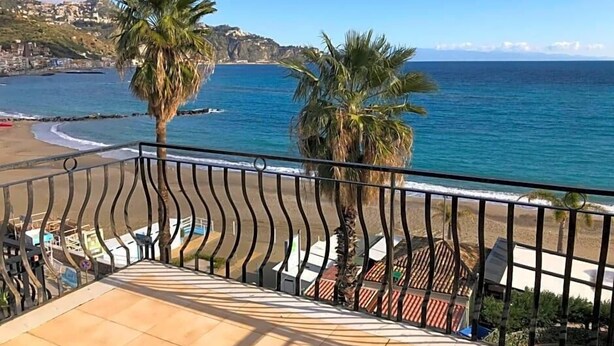 En balkon med udsigt til havet, palmer og fliset gulv.