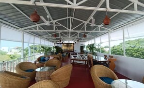 A covered outdoor seating area with wicker furniture, a glass table, and hanging lanterns. - Le Clarisse Guest House (Chennai)