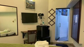 A hotel room with a bed, a TV, a desk, a chair, and a shower area. - Le Clarisse Guest House (Chennai)