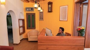 A reception area with a wooden desk, a sofa, and a chair. There are wall-mounted clocks and framed artwork. - Le Clarisse Guest House (Chennai)