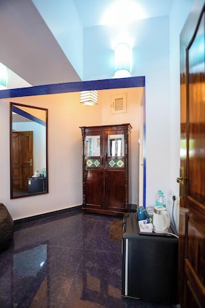 A hotel lobby with a wooden door, a mirror, a light fixture, and a small table with a kettle and water bottles.
