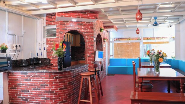 A kitchen with a brick oven, wooden stools, a dining table, and hanging red lanterns. - Le Clarisse Guest House (Chennai)