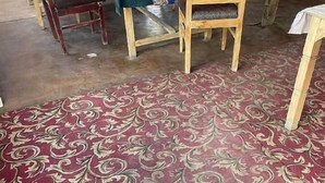 Uma sala de jantar com mesa posta para dois, cadeiras de madeira e um tapete estampado.